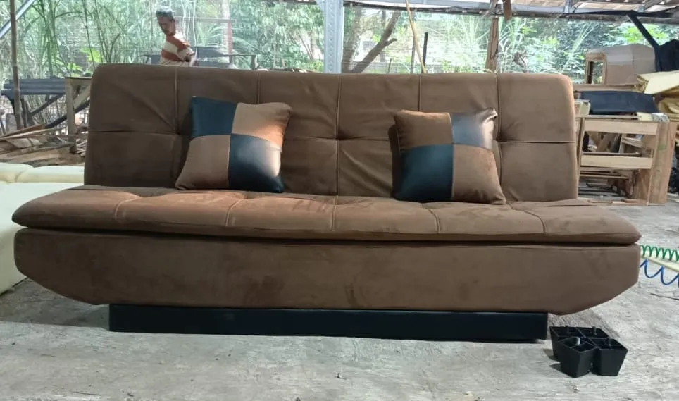 Sofa bed cokelat dengan dua bantal di depan workshop
